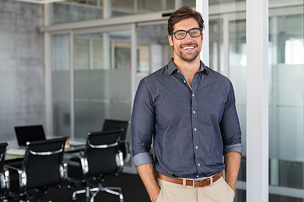 Portrait of young businessman wearing eyeglasses and standing outside conference room